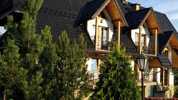 A multi-story building with a sloped roof, wooden balconies, and a well-maintained garden.