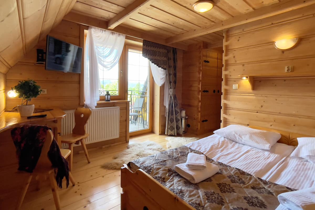 Ein gemütliches Holzblockhaus-Zimmer mit einem Bett, einem Schreibtisch, einem Sessel und einem an der Wand befestigten Fernseher.