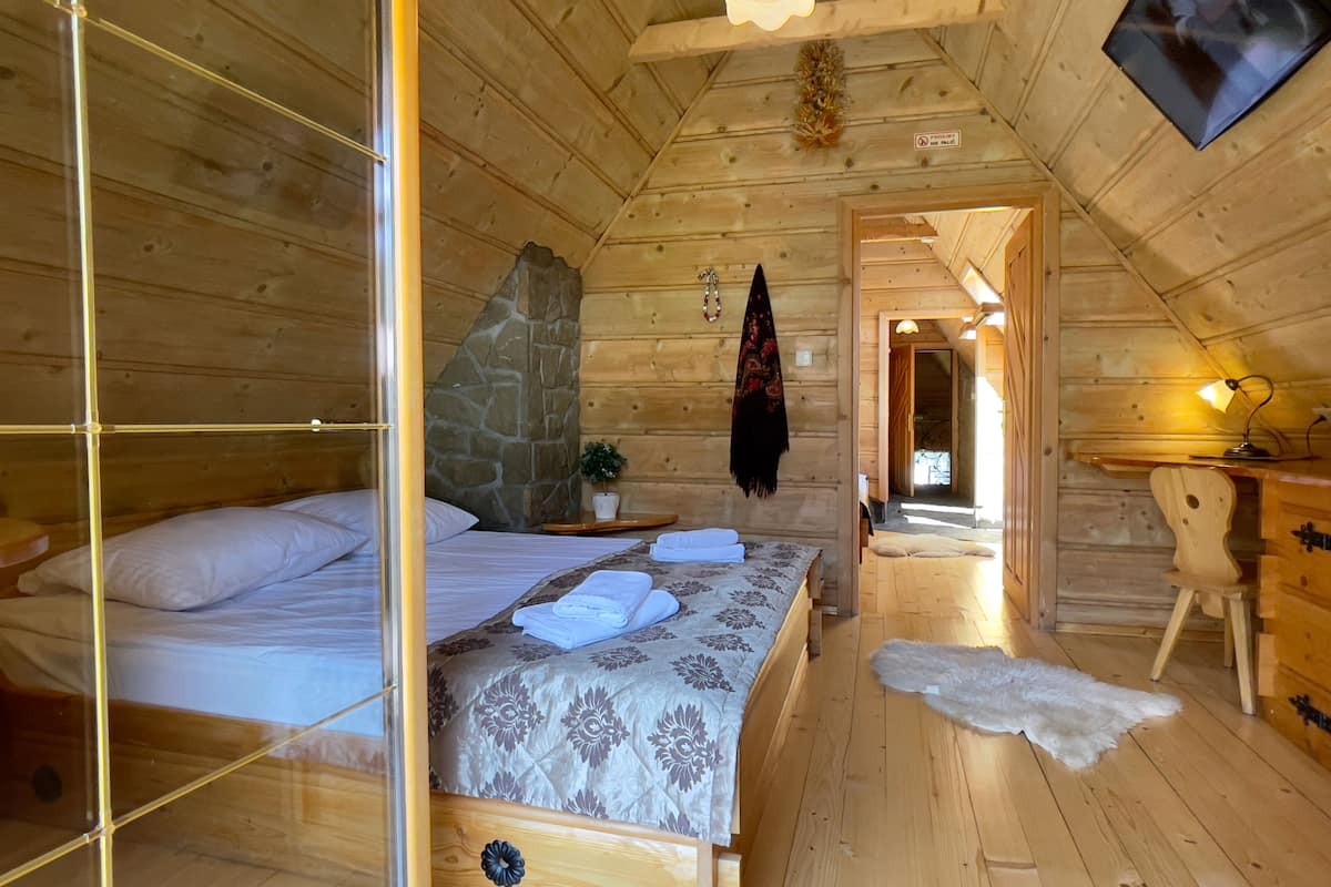Ein Schlafzimmer in einer Holzhütte mit einem Bett, einer Steinwand, einer kleinen Pflanze und einem Schreibtisch mit einer Lampe.
