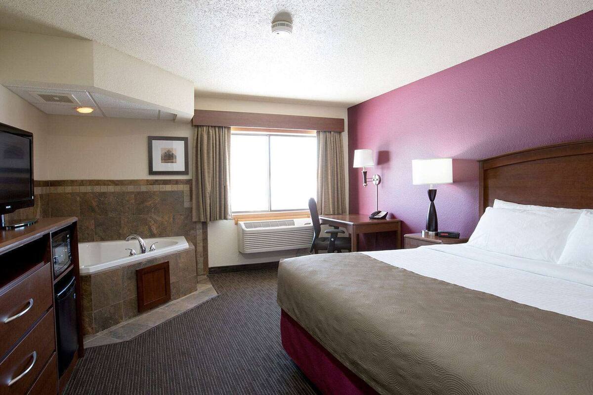 Une chambre d’hôtel comprenant un lit, un bureau, une télévision, une salle de bain avec baignoire et une fenêtre avec des rideaux.