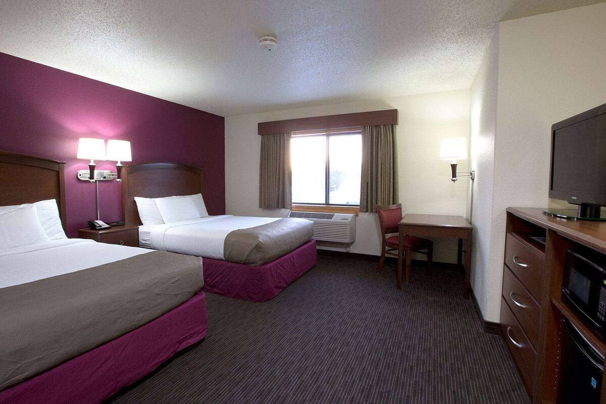 Une chambre d’hôtel avec deux lits, un bureau, une chaise, une télévision et une fenêtre avec des rideaux.