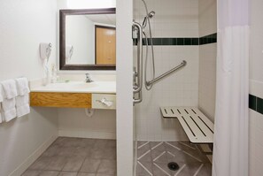 Un baño con lavamanos, espejo, toallero y ducha con barra de apoyo.