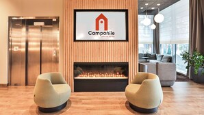 Een moderne lobby met een open haard, twee fauteuils, een lift en een groot raam met uitzicht.