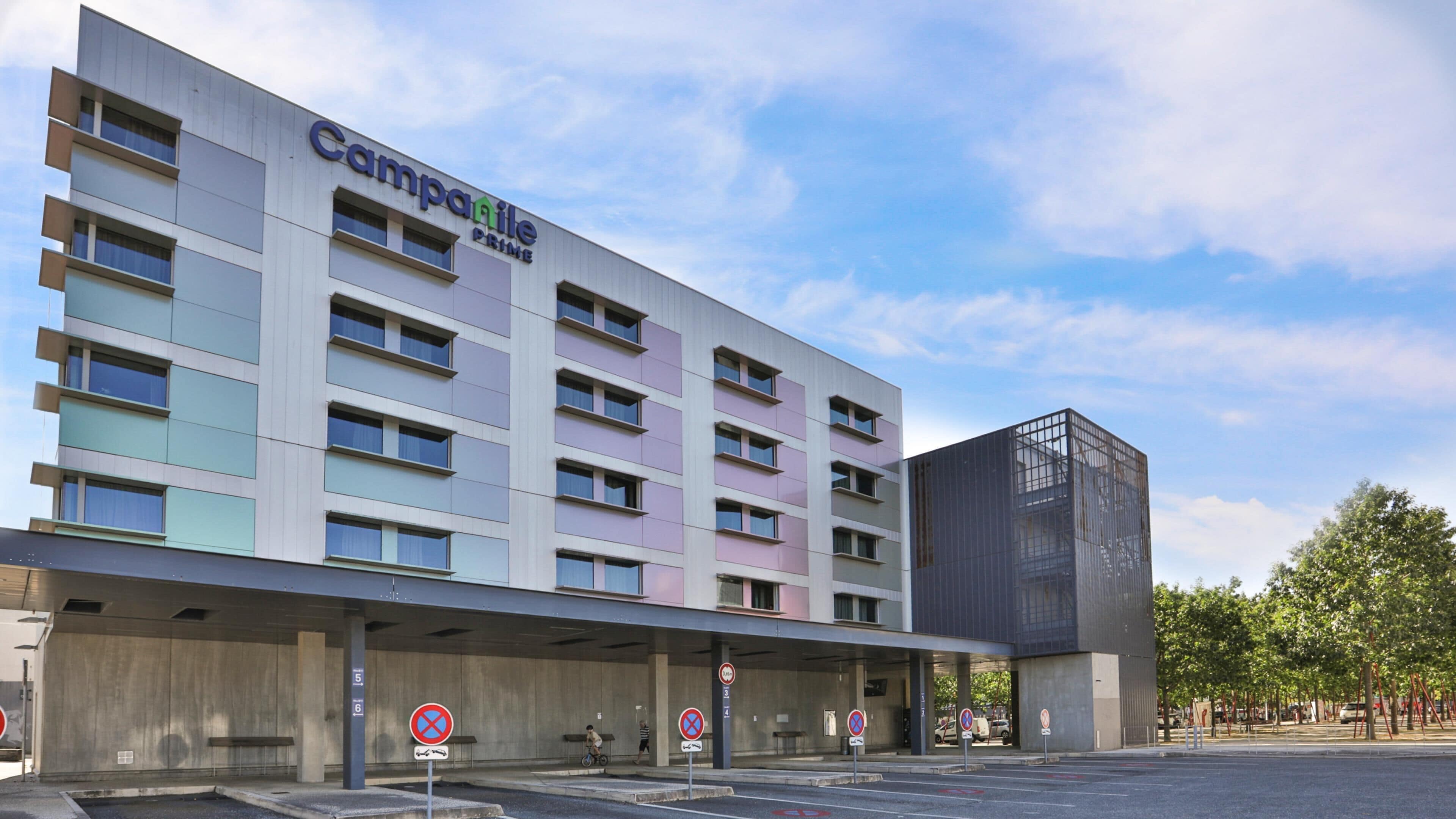 A multi-story hotel with a flat facade, signage for 'Campanile Prime,' and a covered parking area with no parking signs.