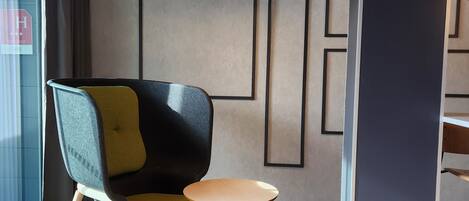 Un interior moderno con un diseño geométrico en la pared, una silla contemporánea y una pequeña mesa redonda.