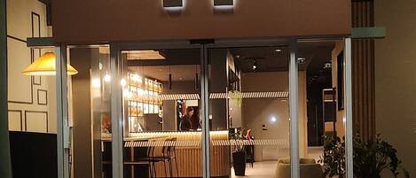 A modern building with a prominent logo above the entrance. Inside, there are wooden tables and chairs, and a bar area with shelves.