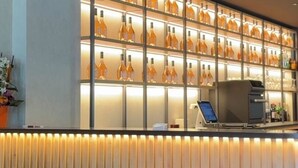 A reception area with a wall of illuminated bottles, a reception desk, and a coffee machine. - Campanile PRIME - La Roche Sur Yon Centre Gare (La Roche-sur-Yon)