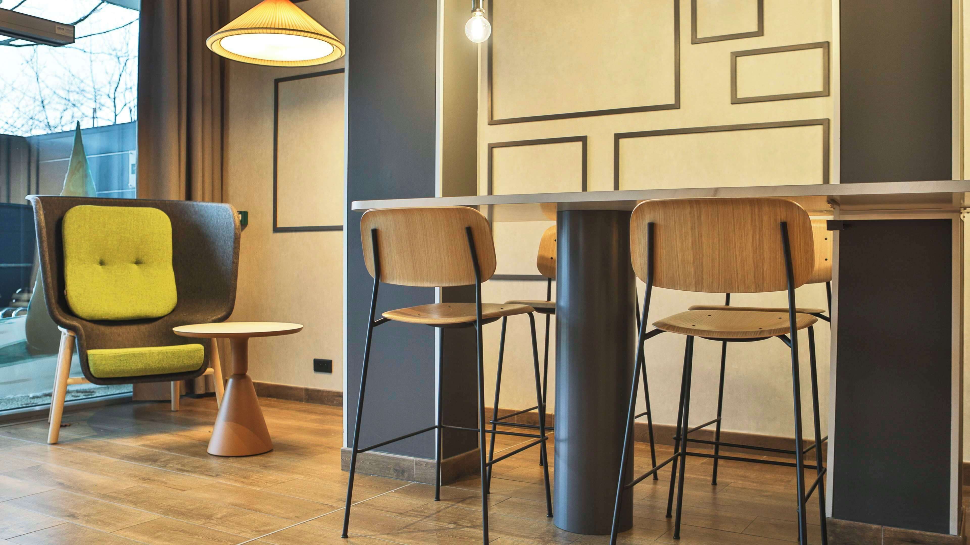Un café moderno con zona de bar, sillas de madera y una butaca tapizada en verde.