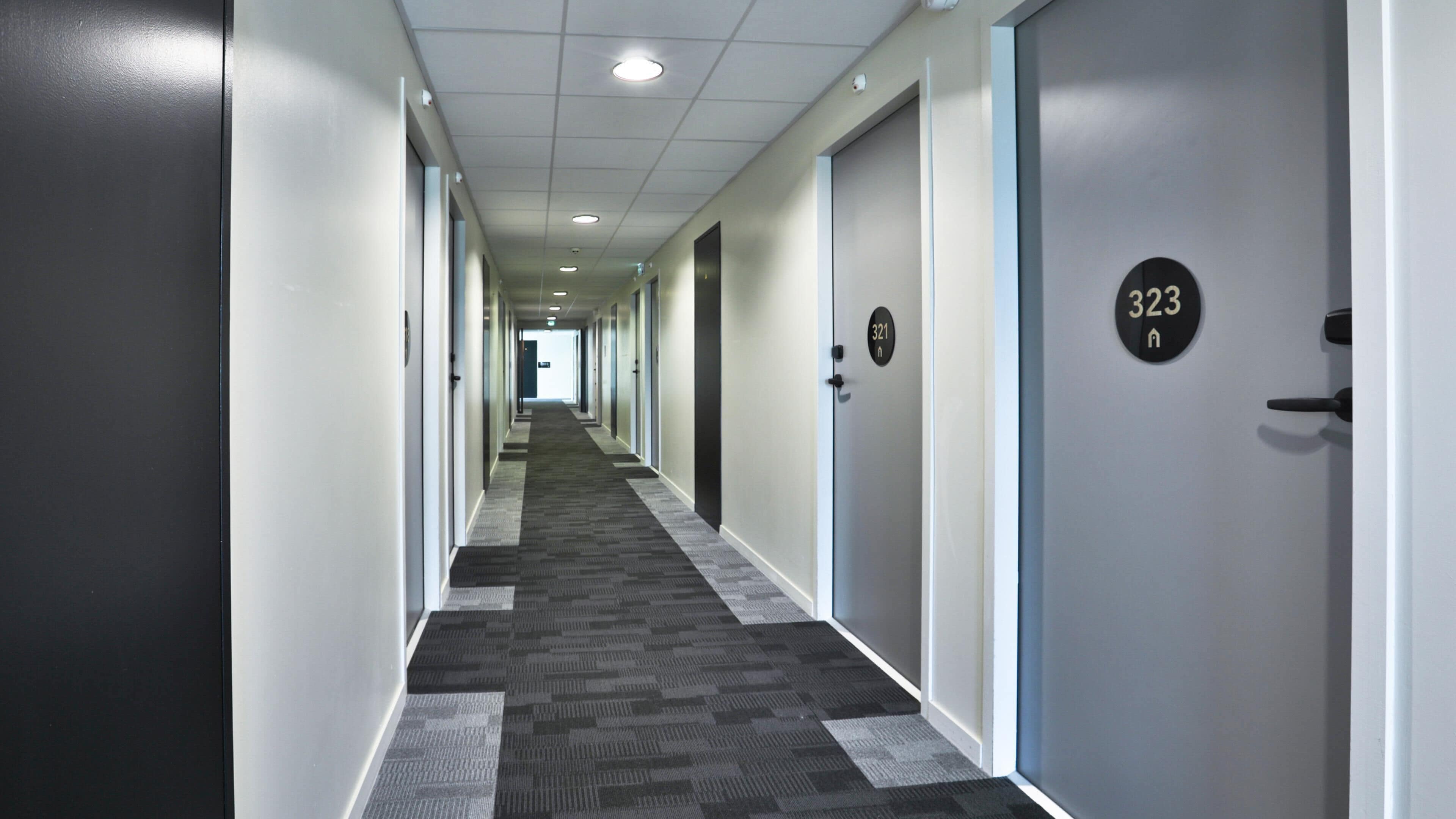 A hotel corridor with doors numbered 321 and 323, carpeted floors, and a ceiling with recessed lighting.