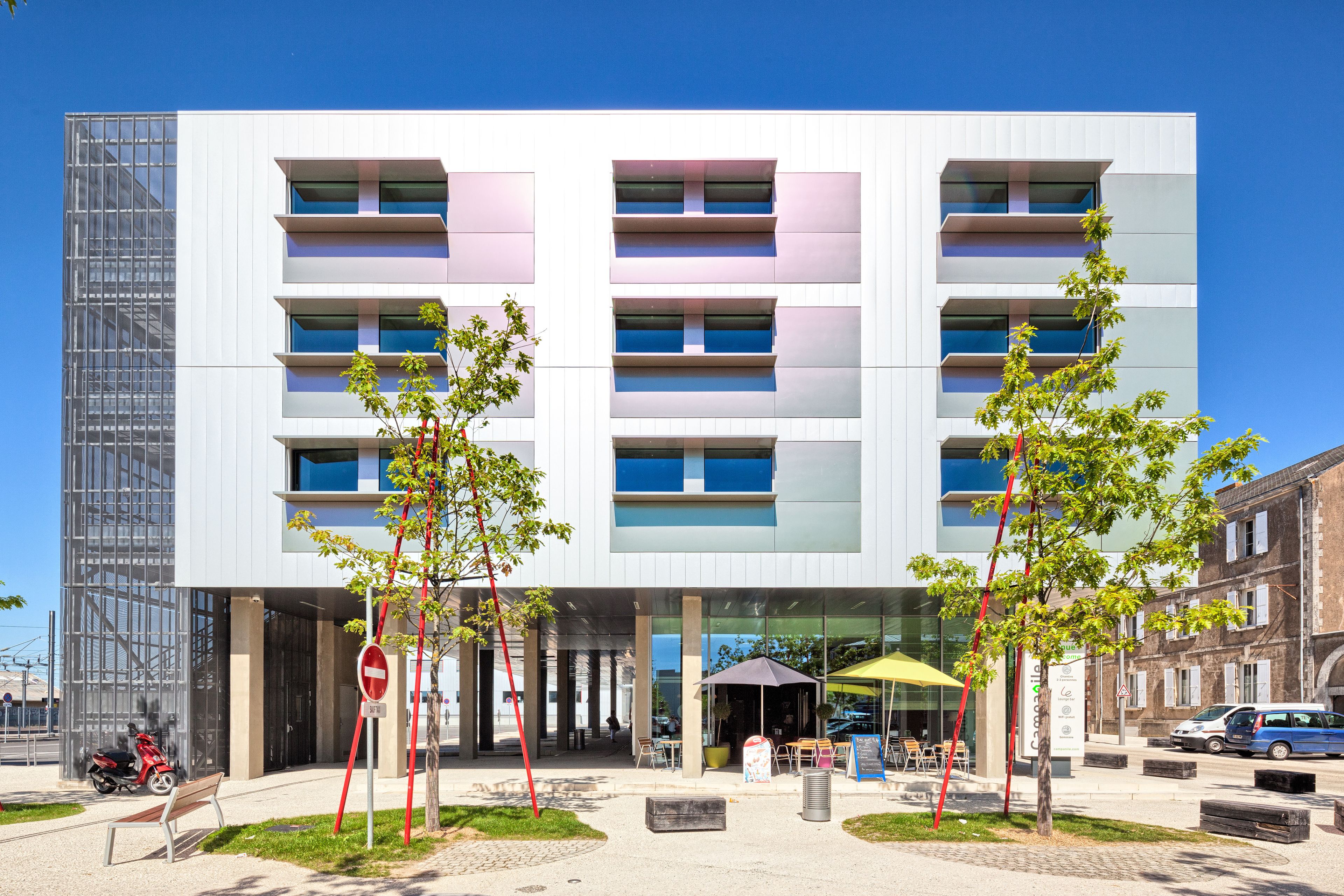 A modern building with multiple floors, outdoor seating, and a clear sky.