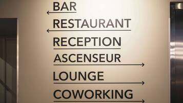 A directional sign with arrows pointing to various locations such as the bar, restaurant, reception, ascenseur, lounge, and coworking area.