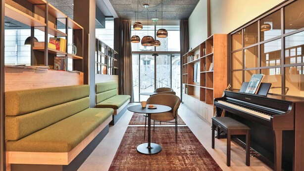 A cozy reading area with a sofa, chairs, a piano, and bookshelves. - Campanile PRIME - La Roche Sur Yon Centre Gare (La Roche-sur-Yon)