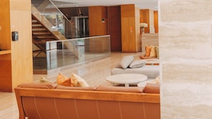 Un interior modern amb una escala de fusta, una zona de seients amb una taula rodona i una barana de vidre.