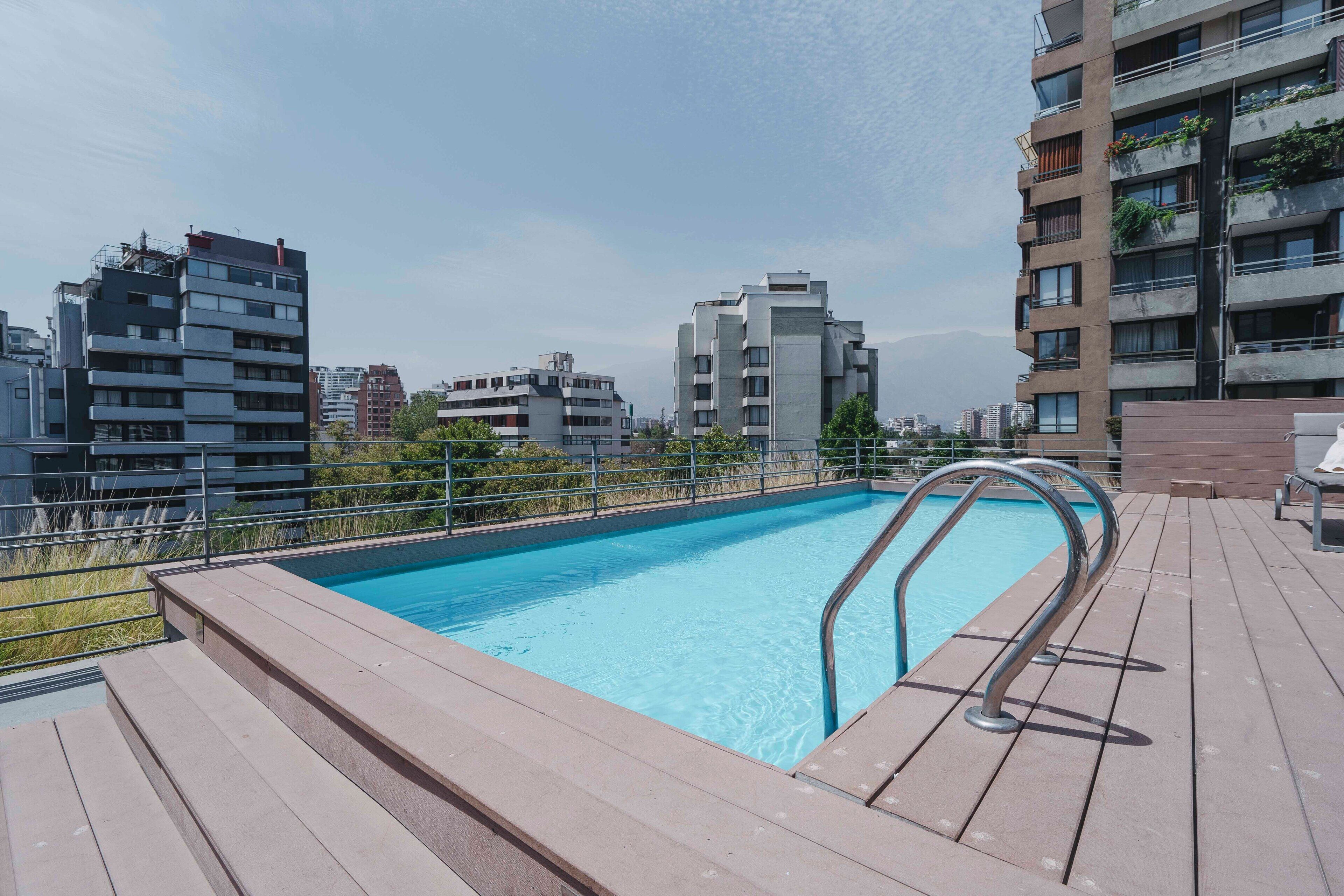 Une piscine sur le toit, dotée d’une terrasse en bois et entourée d’immeubles modernes.
