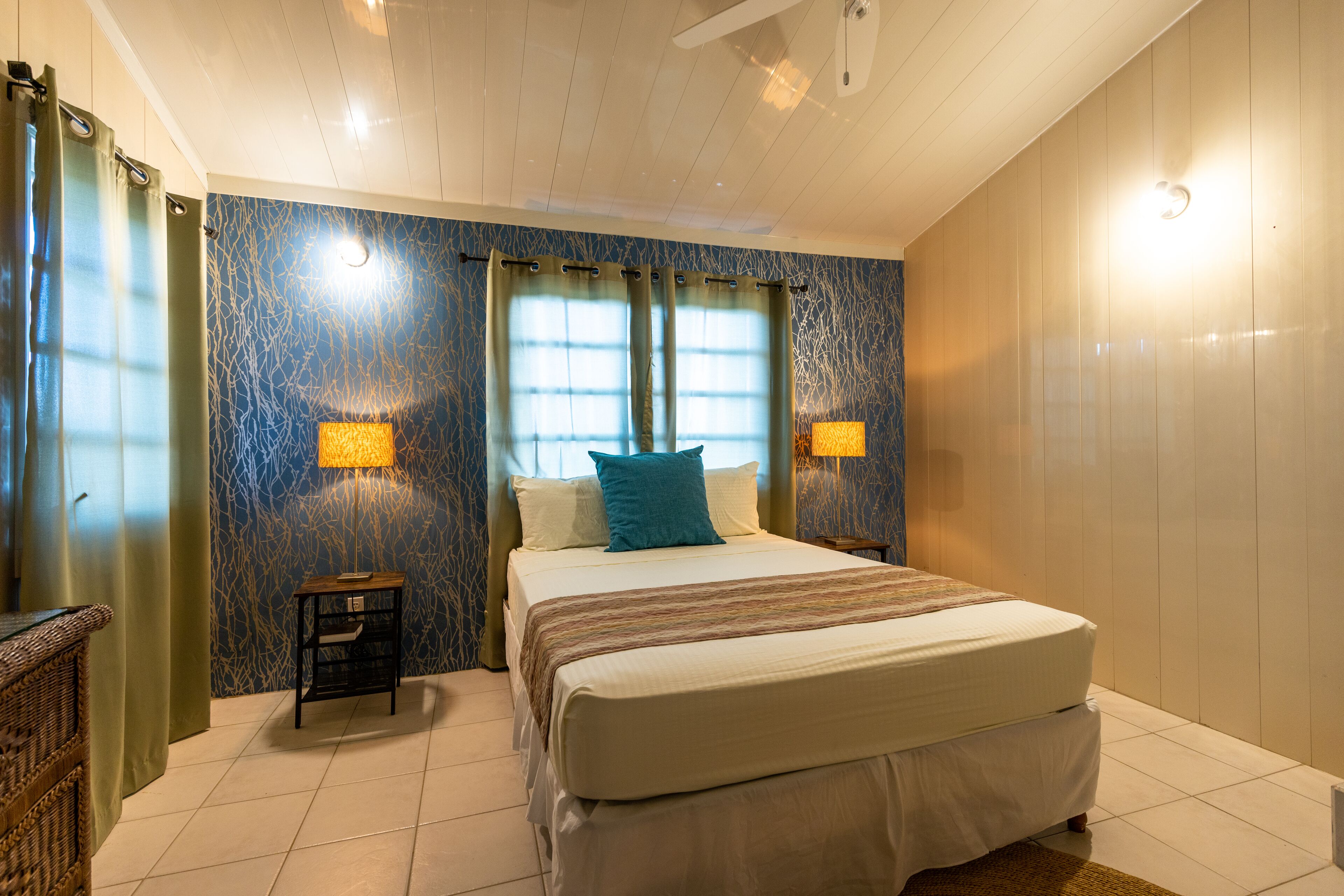 A bedroom with a large bed, two bedside lamps, a nightstand, and a window with curtains.