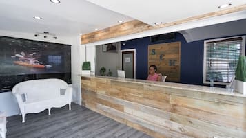 Un área de recepción con un mostrador de madera, un sofá blanco y un ventanal con persianas.