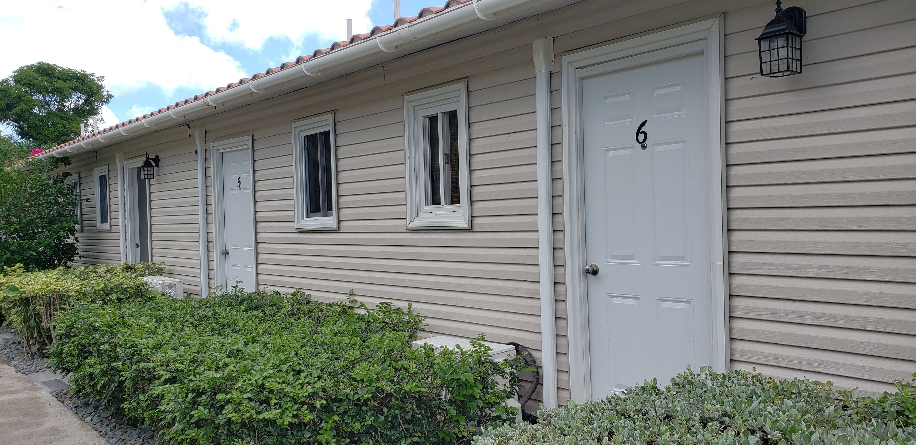 A row of beige wooden houses with white doors, numbered 6, and small windows.