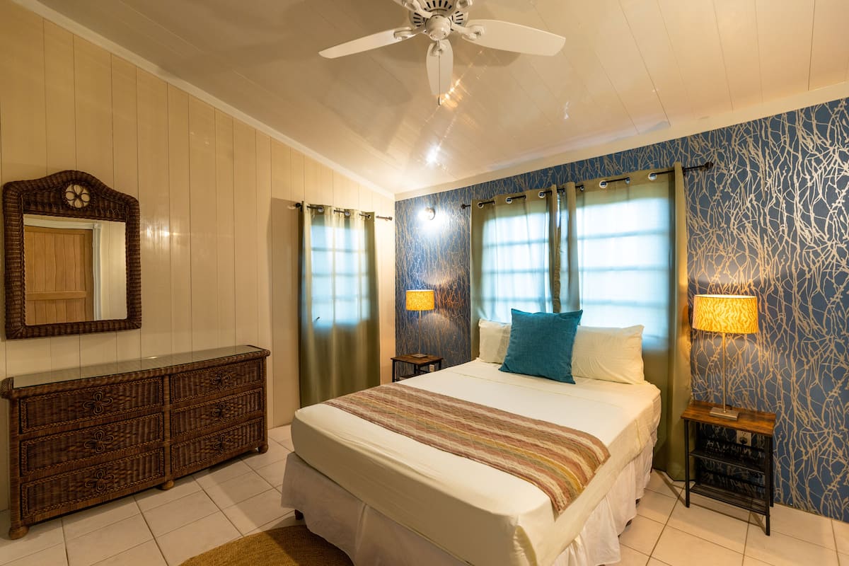 Une chambre à coucher comprenant un lit, une commode, un ventilateur de plafond et deux lampes de chevet.