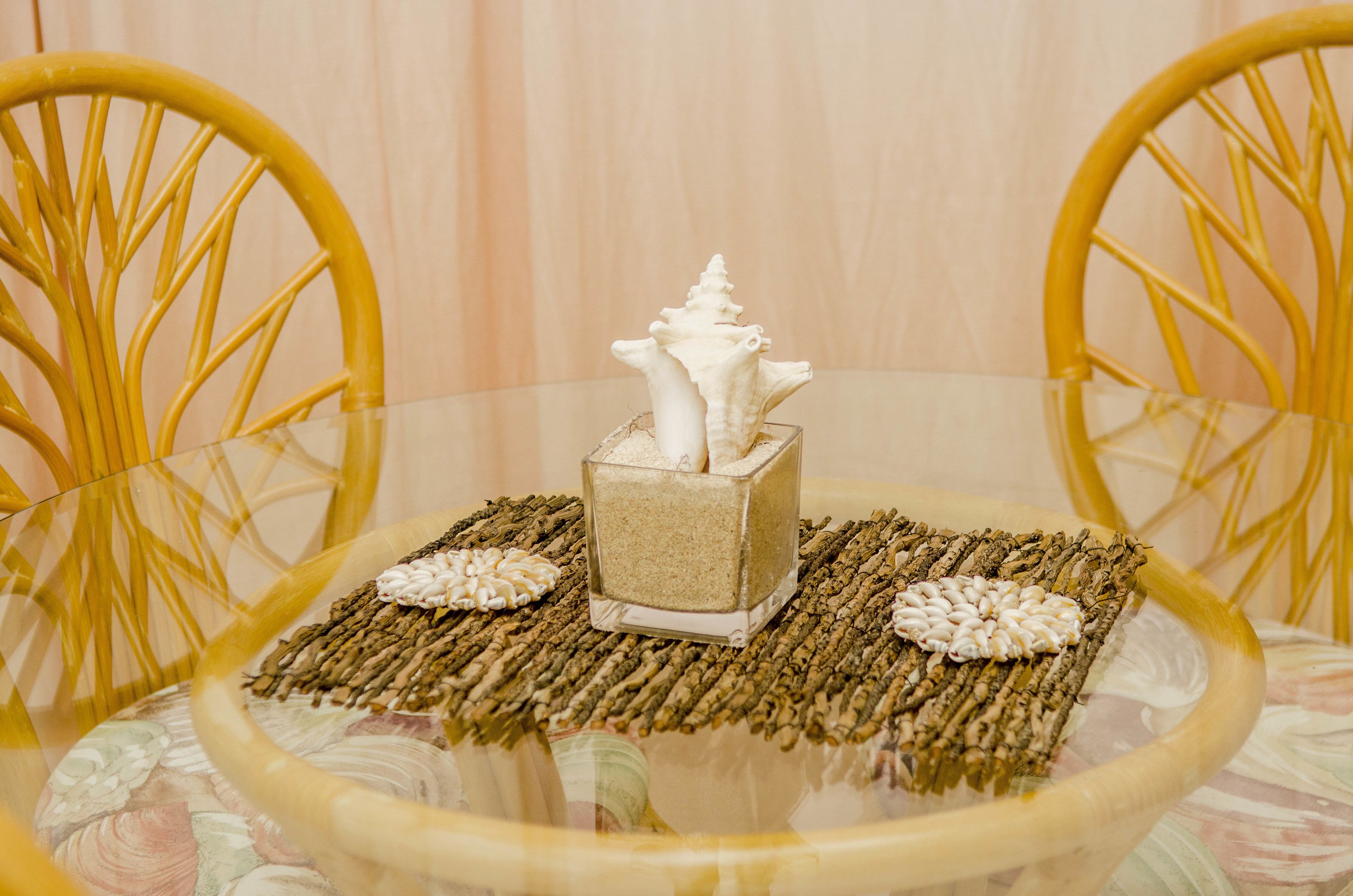 Une table ronde en verre, sur laquelle reposent une boîte à mouchoirs carrée et des objets décoratifs, le tout posé sur un set de table tissé.