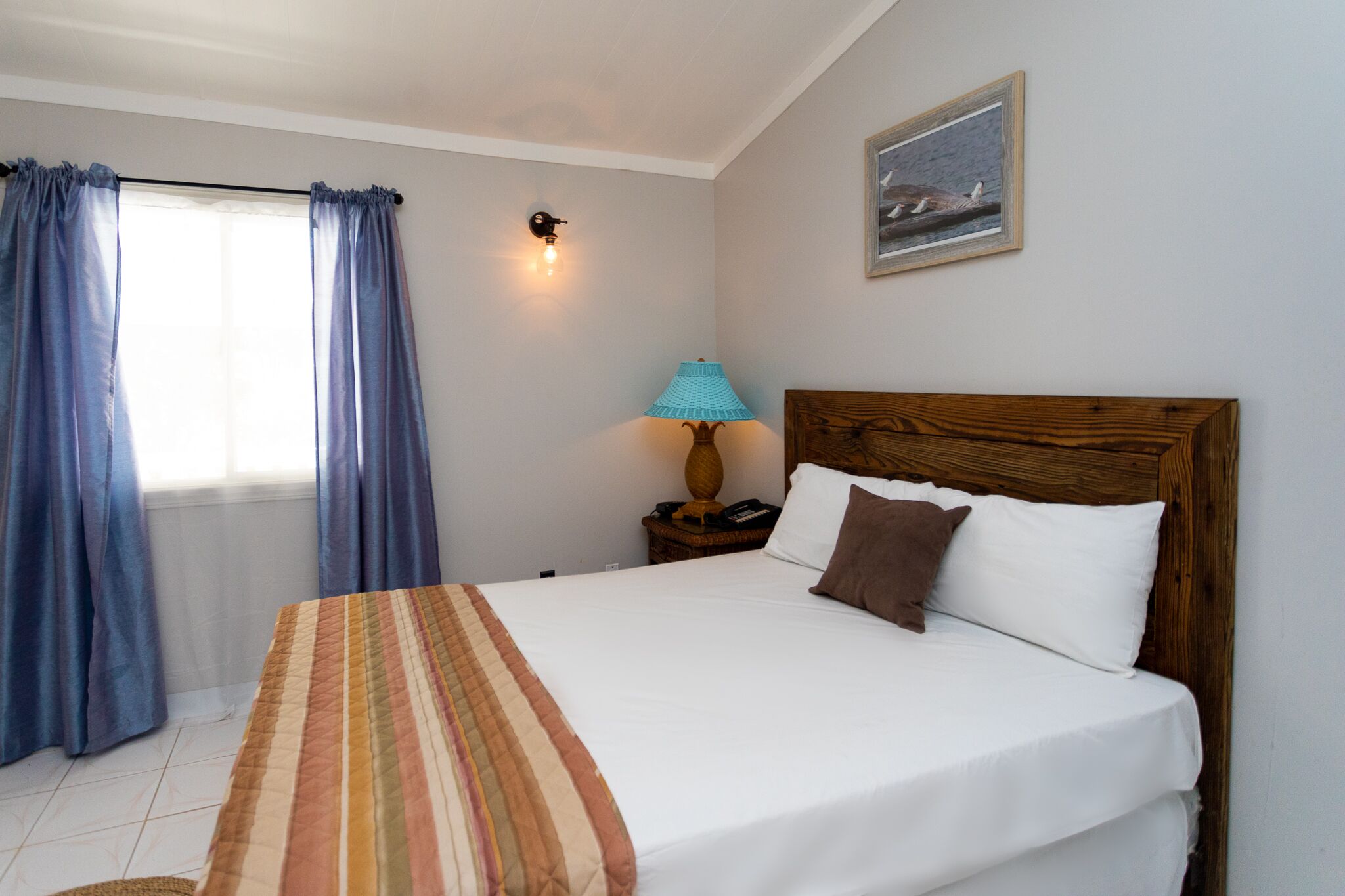 A bedroom with a bed, curtains, a nightstand, a lamp, and a painting on the wall.