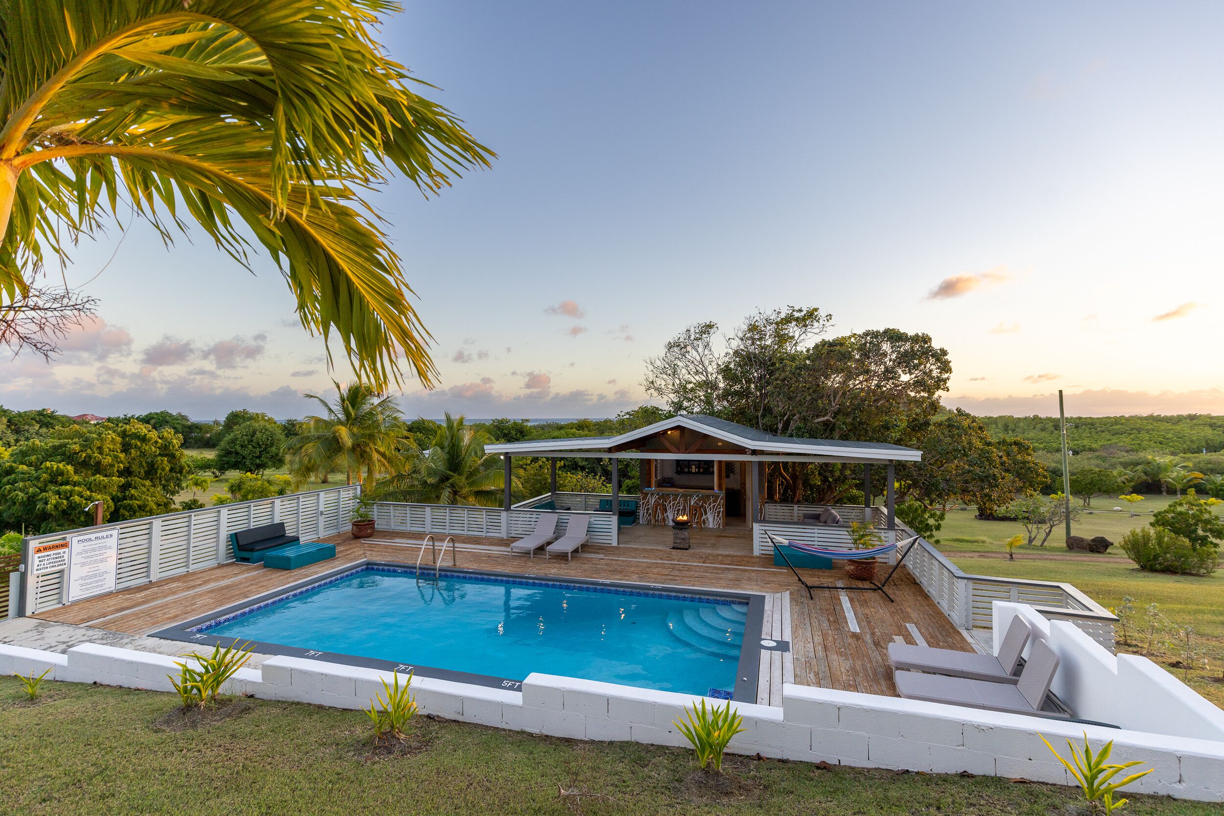 A swimming pool with lounge chairs, a covered seating area, and a view of the surrounding landscape.