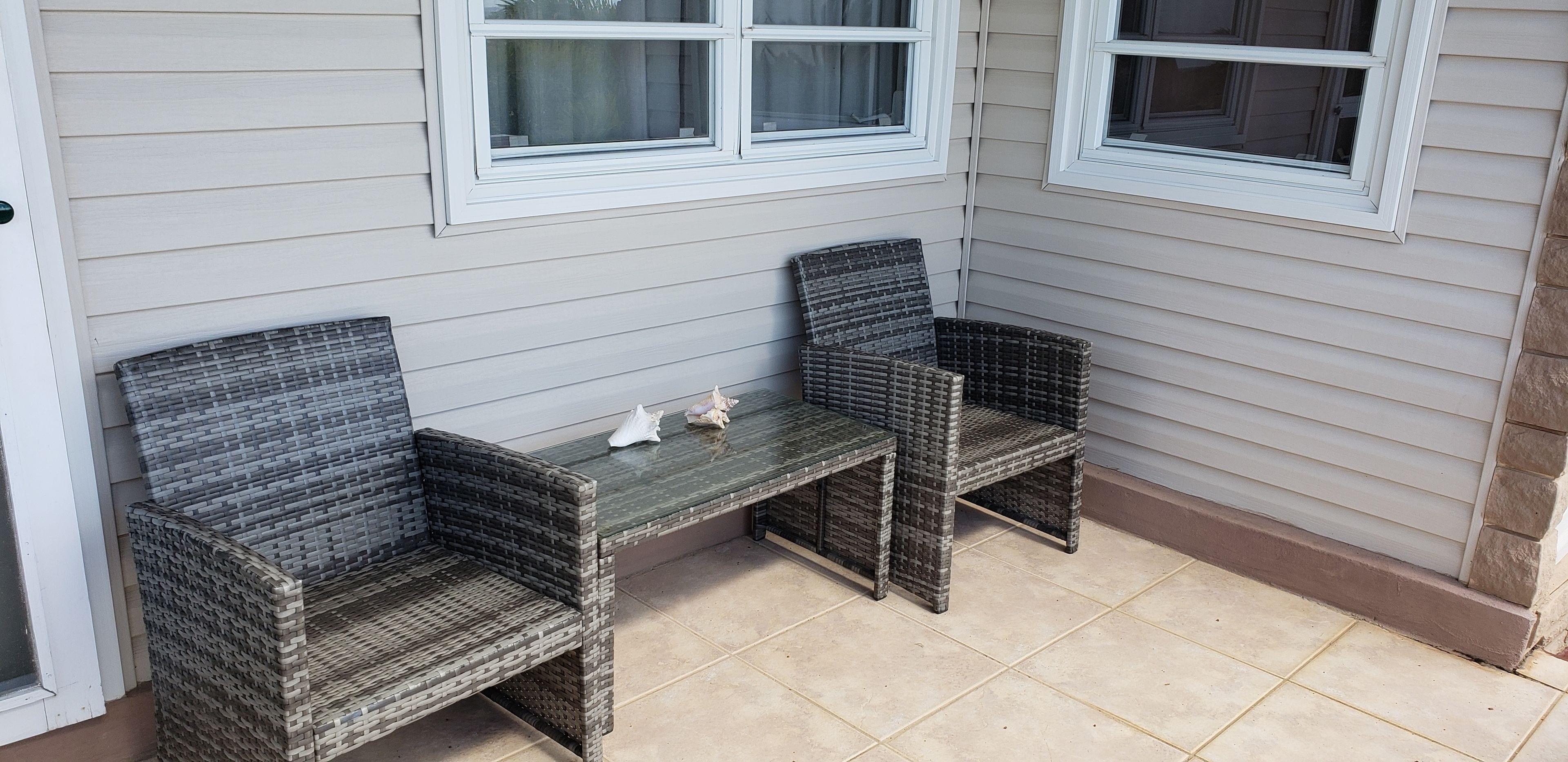 A corner seating area with wicker chairs and a small table, against a light-colored wall with windows.