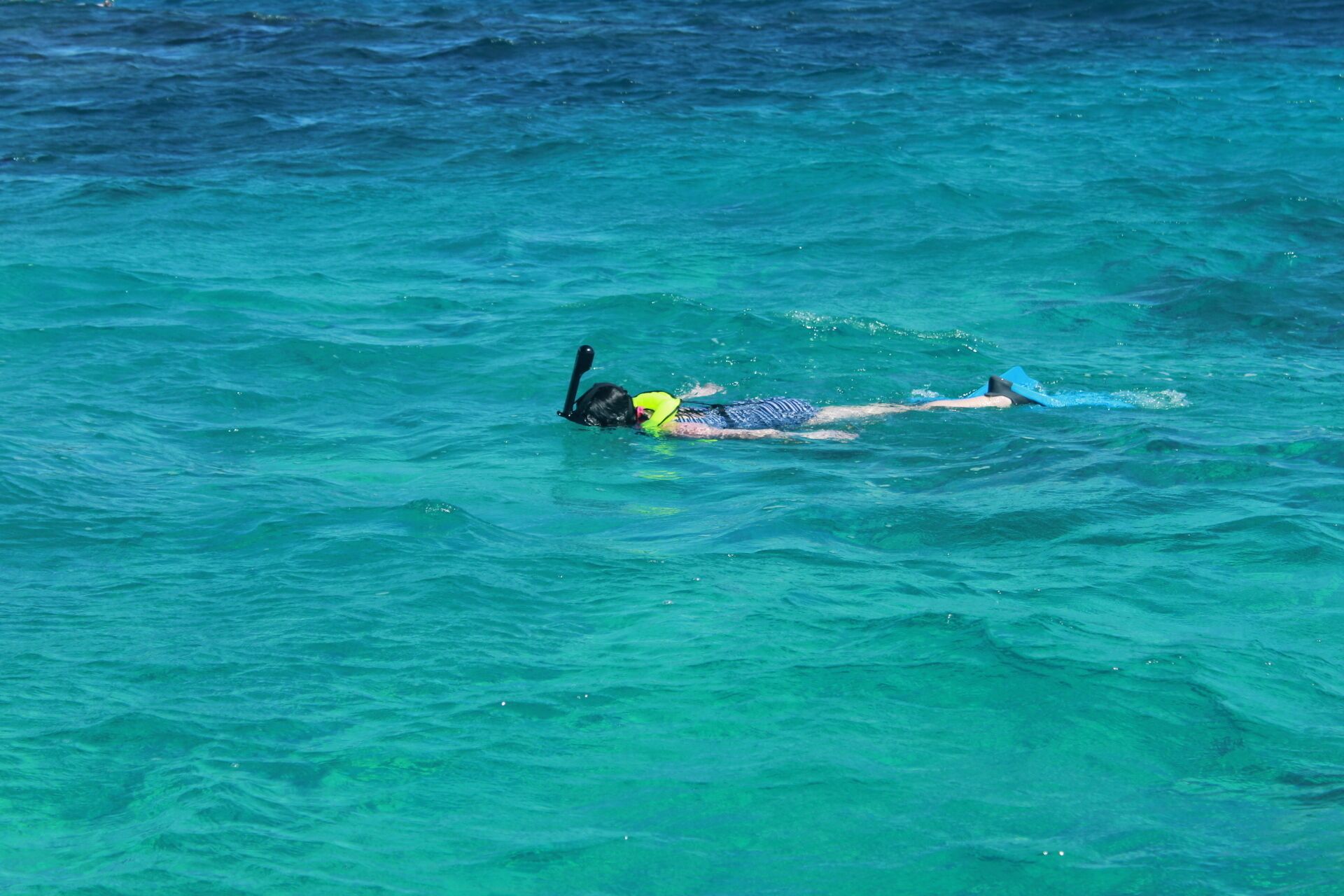 Une personne nage dans une eau d’un bleu cristallin.