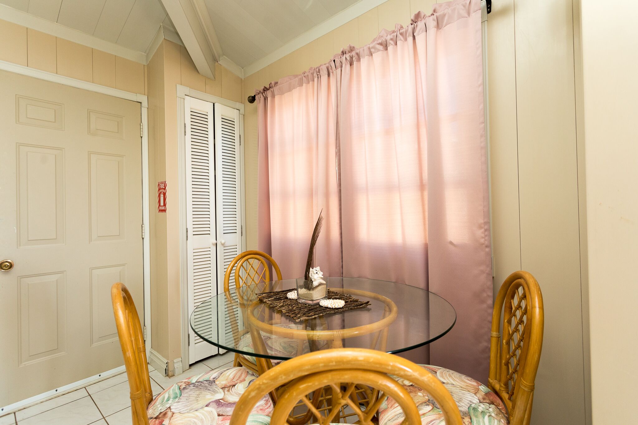 A dining area with a glass table, wicker chairs, a decorative cake, and a door with louvered shutters.