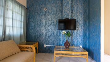 A room with a sofa, a glass-top table, a TV mounted on the wall, and a patterned blue wall.