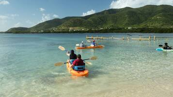 Personas haciendo kayak en un cuerpo de agua tranquilo y cristalino, con montañas al fondo.