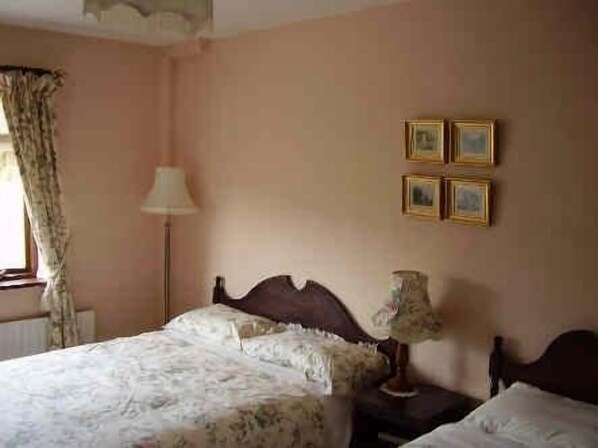 A bedroom with a bed, a nightstand, a lamp, and a window with curtains.