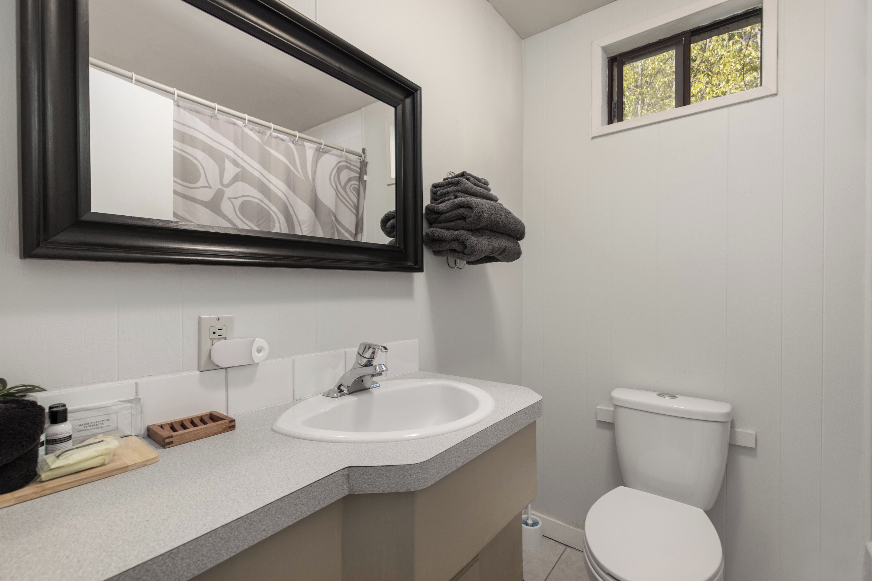 A bathroom with a white sink, a mirror, a toilet, and a window.