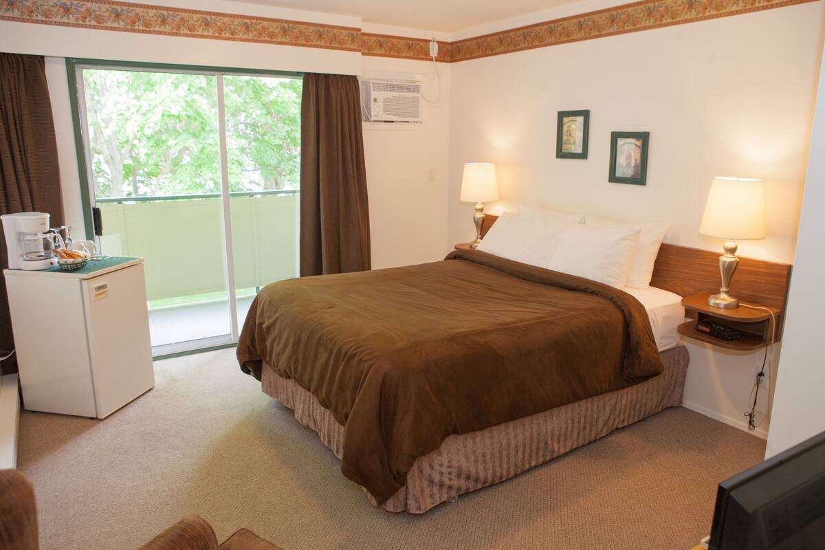 Habitación de hotel con cama, dos lámparas de noche, una mesita con cafetera y vistas al verdor por la ventana.