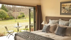 Une chambre avec un grand lit, deux lampes de chevet, un tableau encadré au mur et une vue sur le jardin par une porte ouverte.