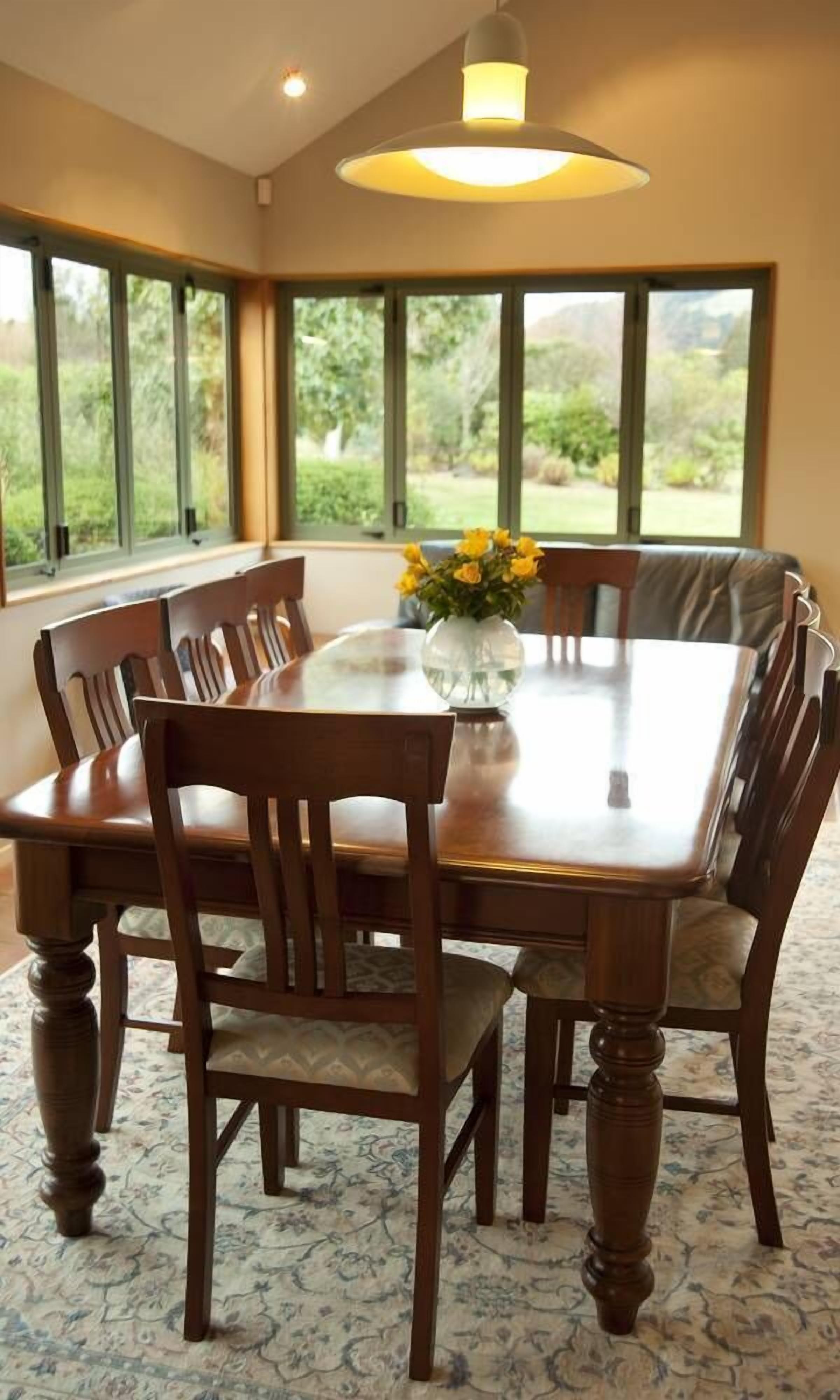 Un comedor con una mesa grande, sillas de madera y un jarrón de flores amarillas.