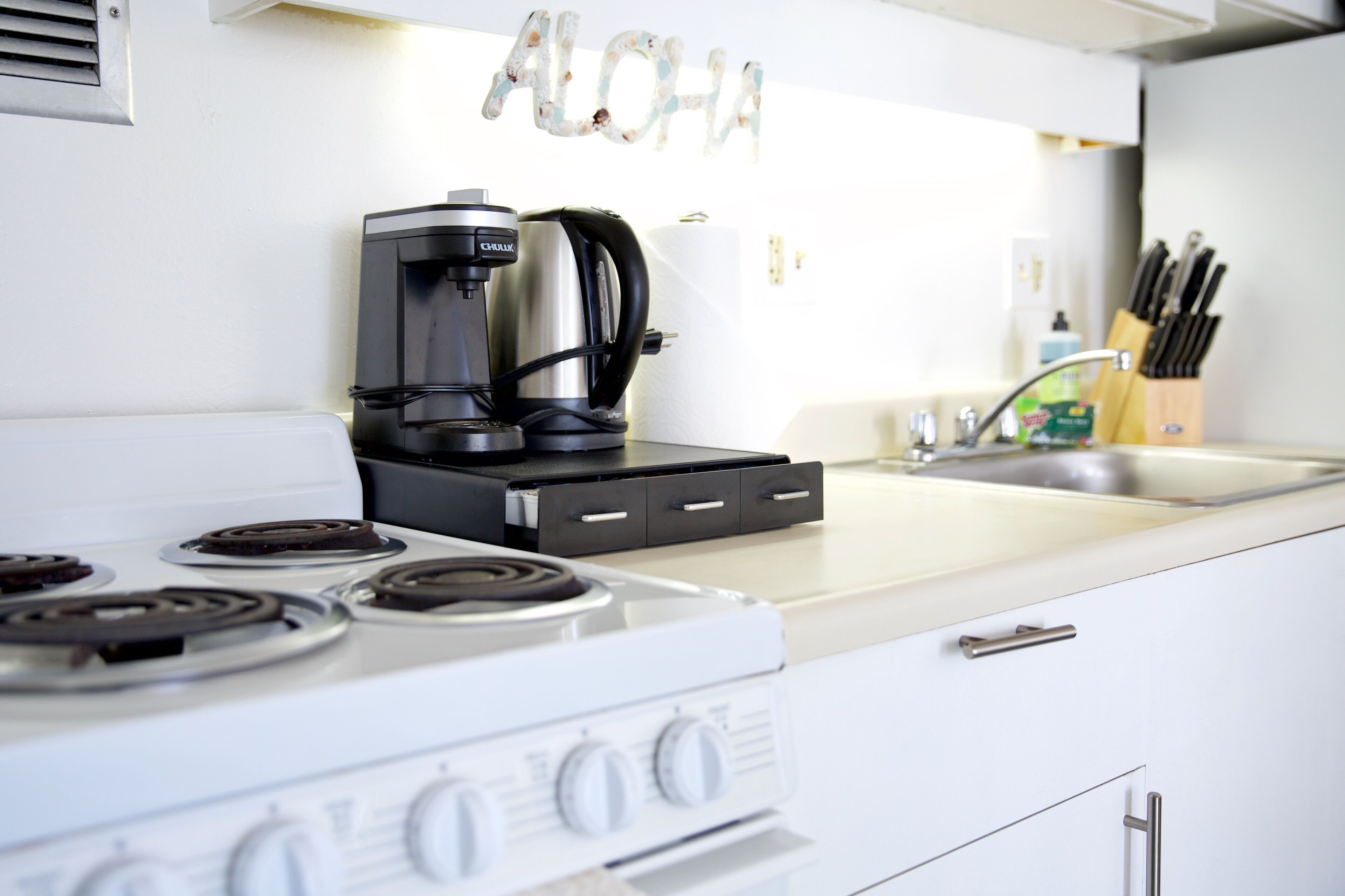 A kitchen with a coffee maker, a stove, and a sink.