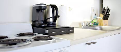 A kitchen with a coffee maker, a stove, and a sink.