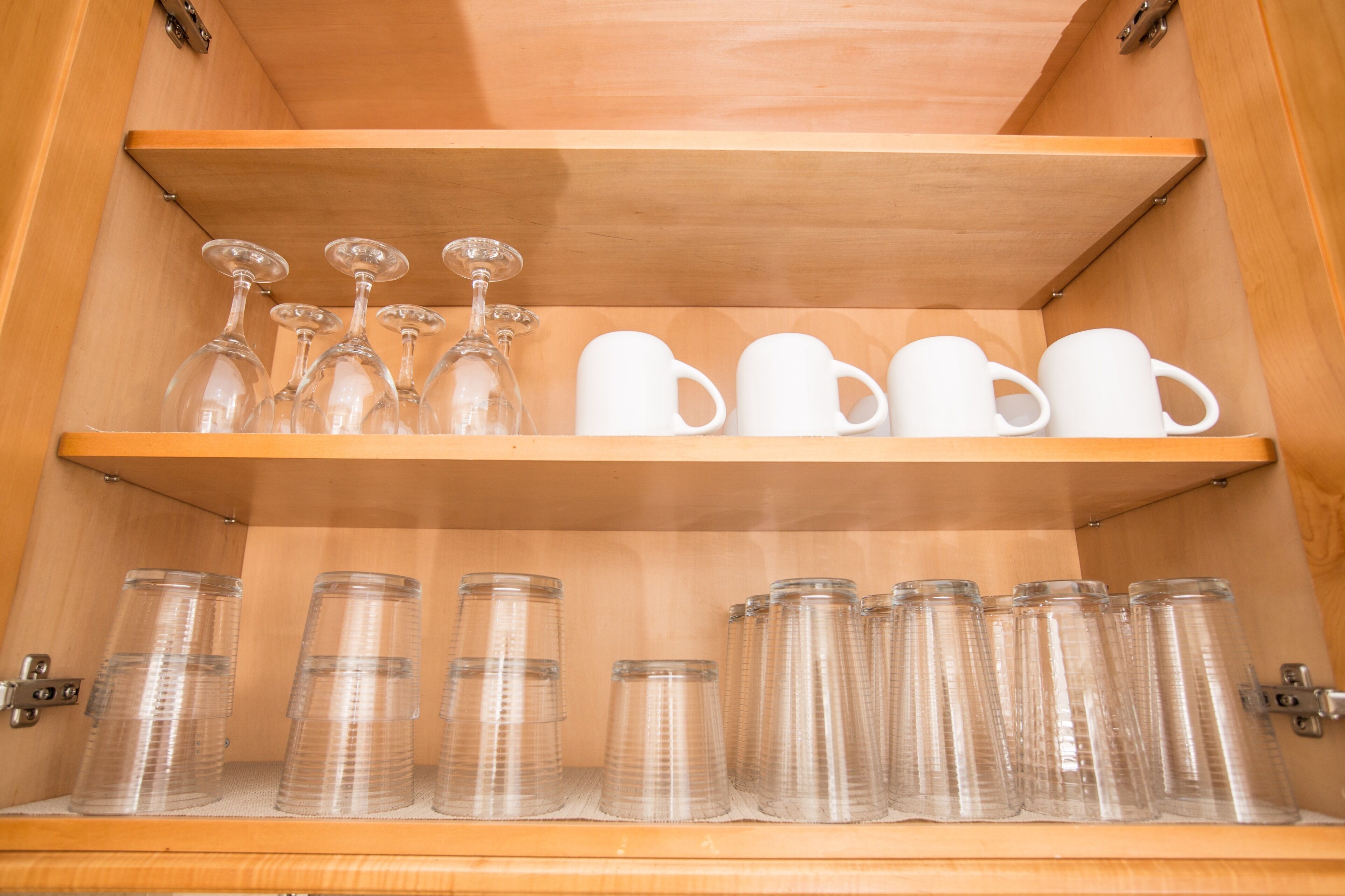 A wooden cabinet with shelves holding clear glassware and white mugs.