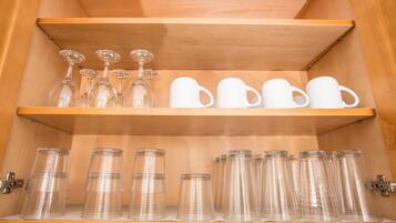 A wooden cabinet with shelves holding clear glassware and white mugs.