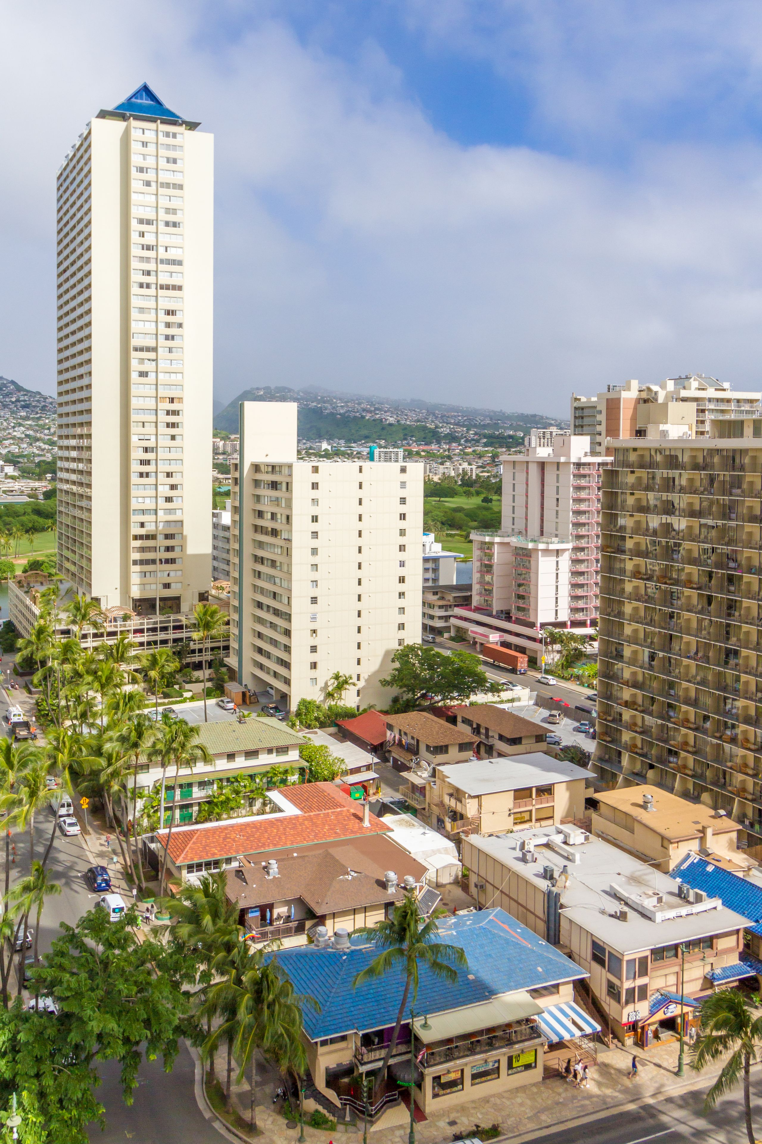 A high-rise hotel with multiple floors, surrounded by other buildings and palm trees.