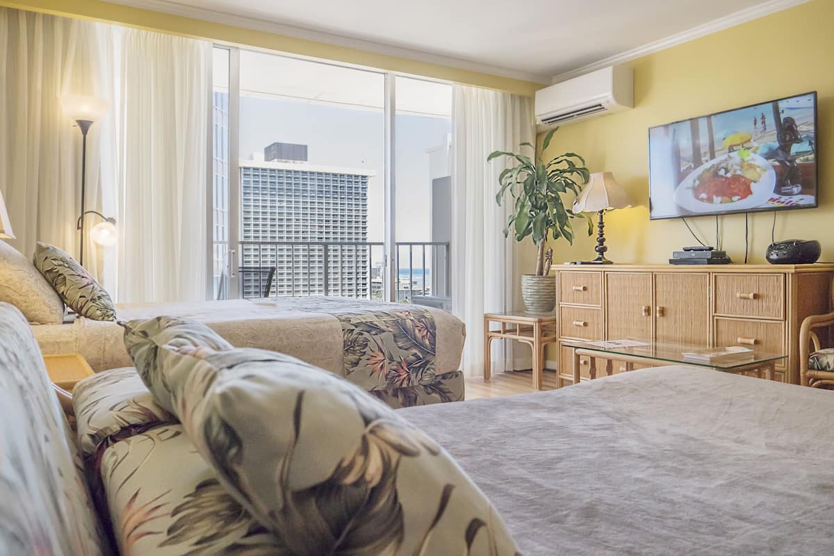 Hotellihuone, jossa on kaksi sänkyä, televisio, työpöytä ja näkymä kaupunkiin.