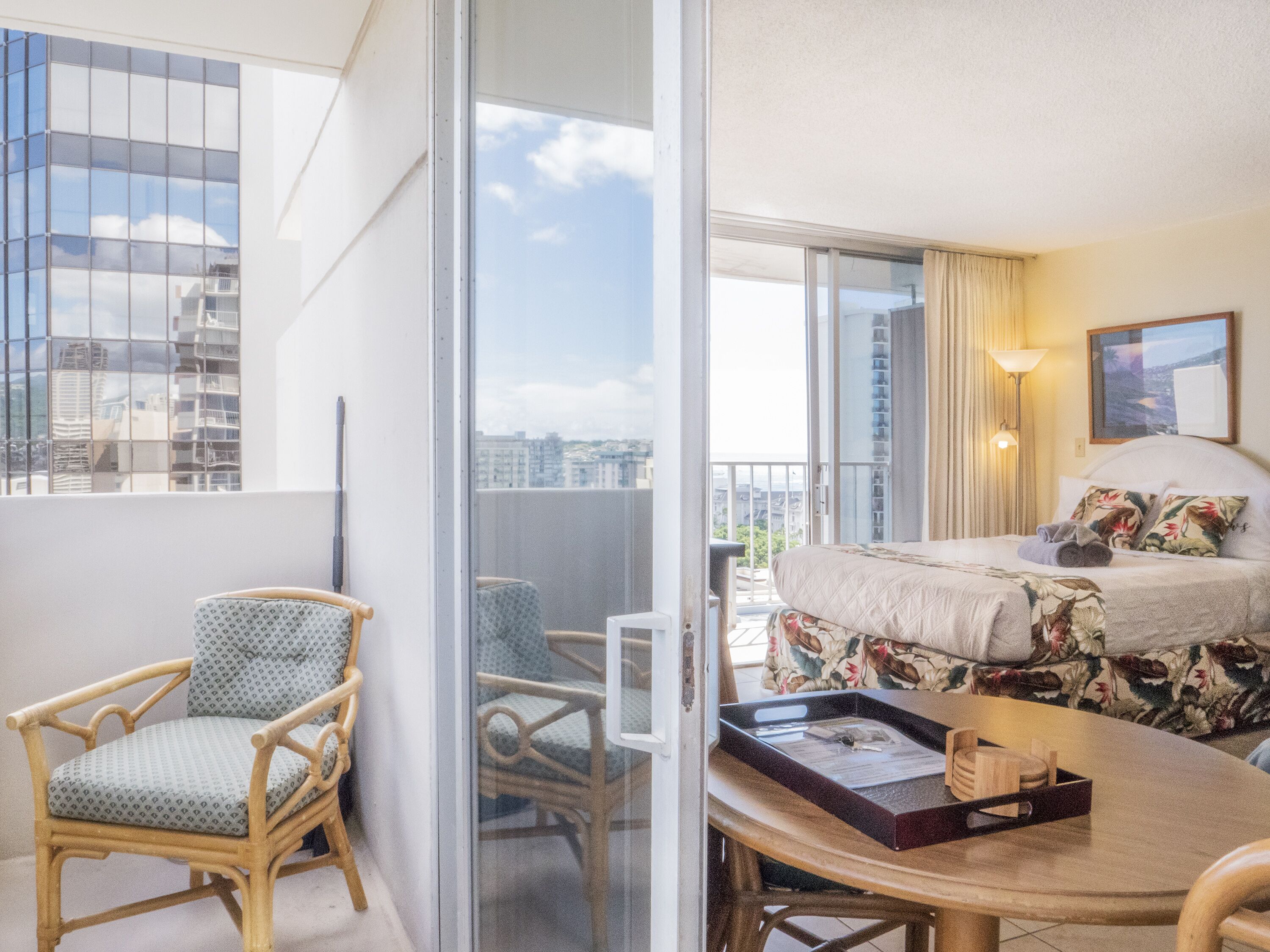 Habitación de hotel con cama, una silla, una mesa y vistas de la ciudad a través de amplios ventanales.