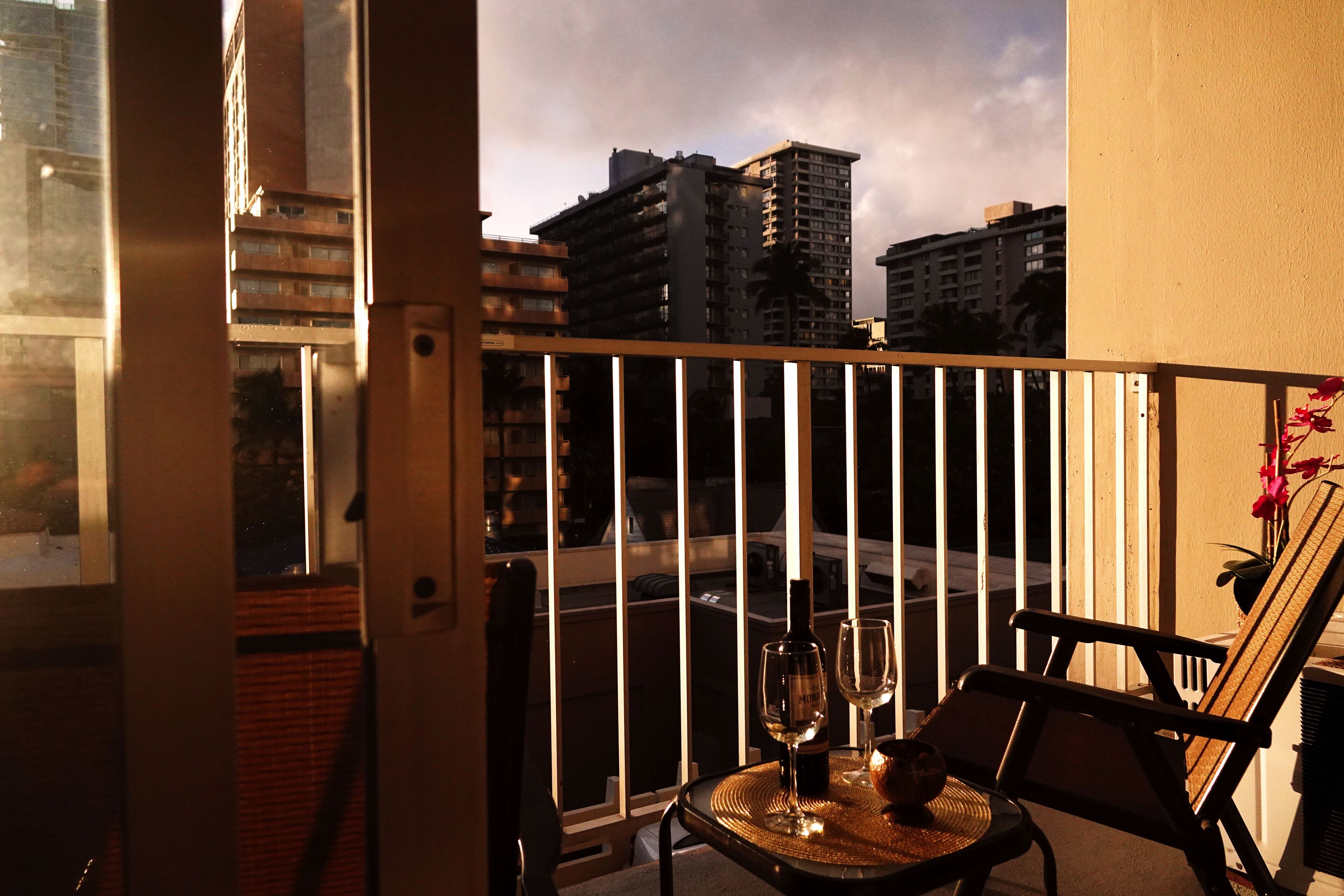 A balcony with a view of tall buildings, a table with a bottle and glass, and a chair.