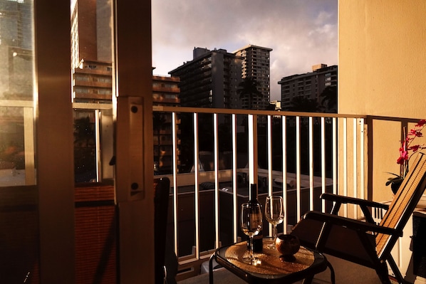 A balcony with a view of tall buildings, a table with a bottle and glass, and a chair.