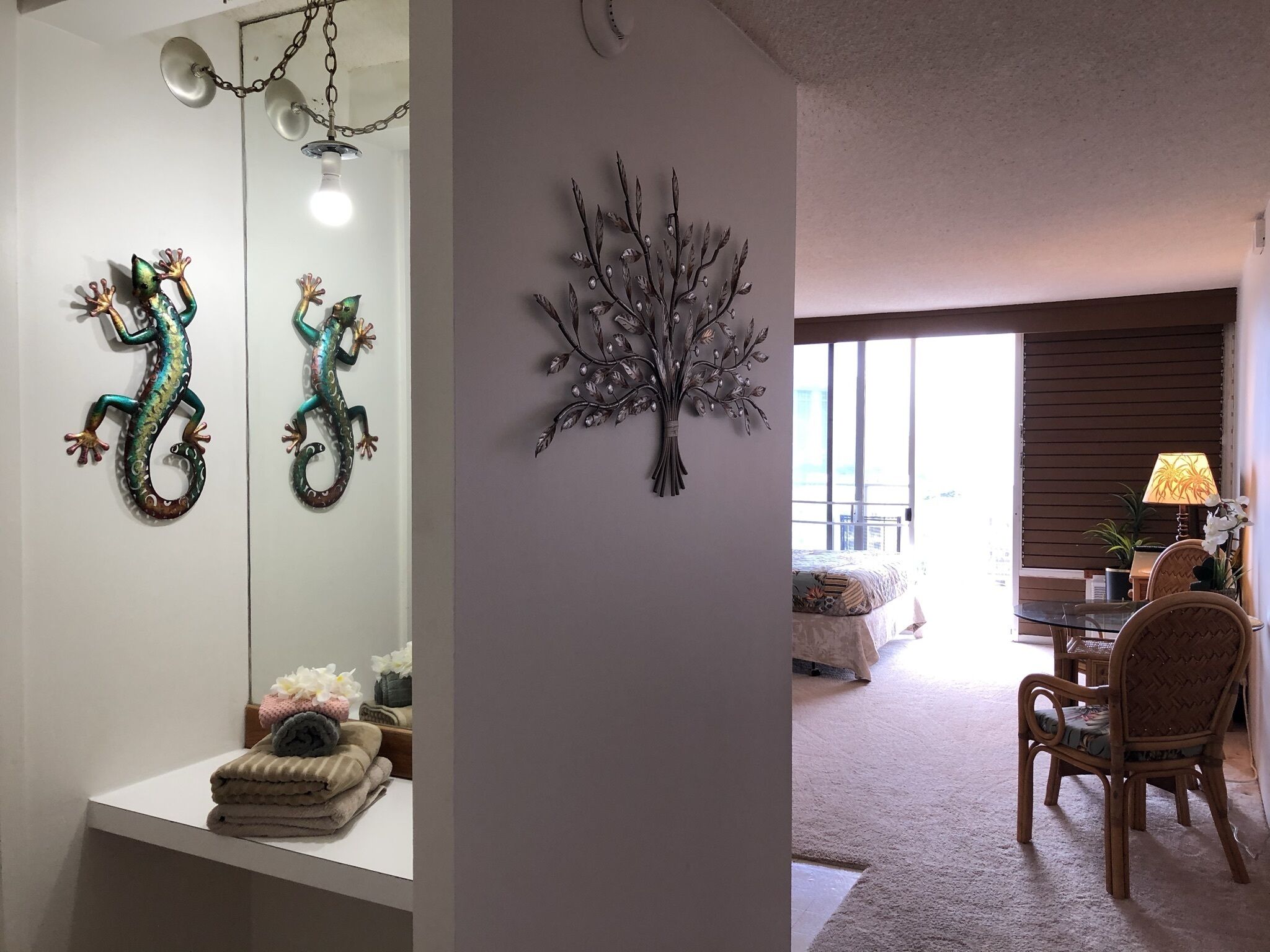 A bathroom with a mirror, two decorative lizards, a wall-mounted tree branch, and a towel rack with folded towels.