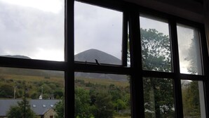 A room with a large window offering a view of a rural landscape, including a stone wall, green fields, and a distant mountain.