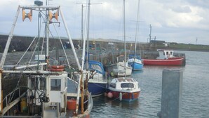 A harbor with several boats docked, including a fishing boat with equipment and a smaller boat with a cabin.