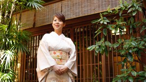 Un edificio japonés tradicional con ventanas de celosía de madera y un jardín con follaje verde.