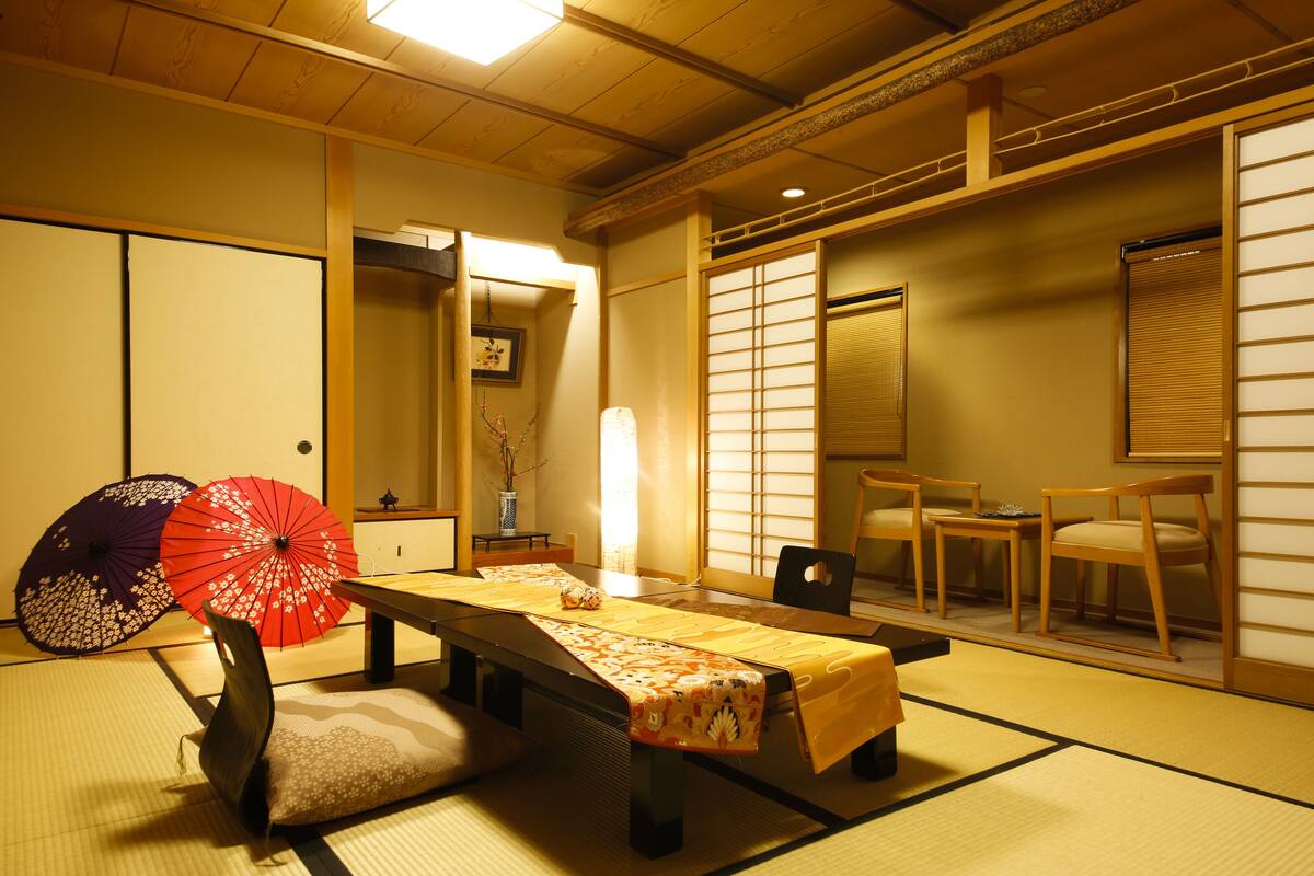 Una habitación japonesa tradicional con suelo de tatami, una mesa baja con camino de mesa y dos paraguas.