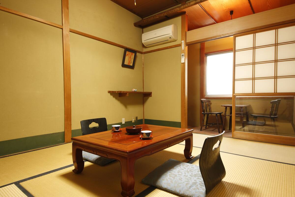 Una habitación japonesa tradicional con suelo de tatami, una mesa de madera con juego de té y puertas correderas que dan a un balcón.
